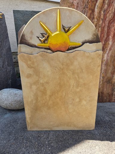 Ein Grabstein mit Sonnensymbol und stilisierten Wellen.