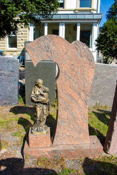 Grabstein mit einer Statue eines Kindes, umgeben von grauen Edelsteinen.