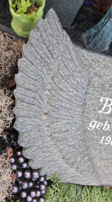 Granitgrabstein mit Flügel-Motiv und der Inschrift „Er, geboren 19XX“.