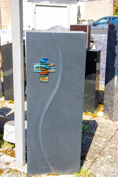 Dunkelgrauer Grabstein mit geschwungener Linie und farbiger Dekoration.