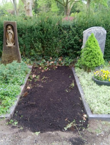 Ein angelegtes Grab mit einer Statue und zwei Gräbern in einer grünen Umgebung.