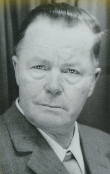 Ein älterer Mann mit ernstem Gesichtsausdruck und einem Anzug.