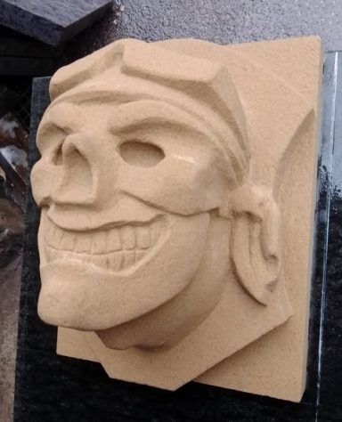 Skulptur eines grinsenden Schädelgesichts mit markanten Zügen.