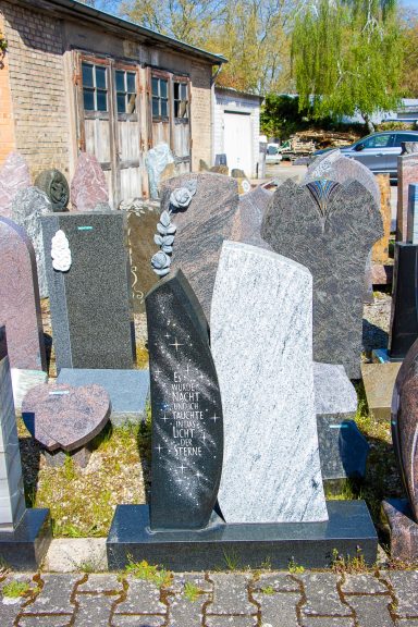 Zwei Grabsteine aus unterschiedlichen Steinarten stehen auf einem Friedhof.