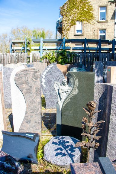 Granitsteine in einem Friedhof, mit verschiedenen Designs und einem blauen Himmel im Hintergrund.