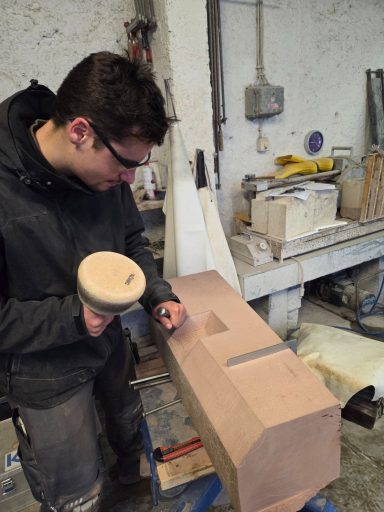 Junger Handwerker bearbeitet einen Holzblock mit einem Werkzeug in einer Werkstatt.