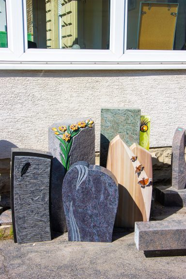 Eine Gruppe von Grabsteinen in verschiedenen Formen und Farben vor einer Wand.