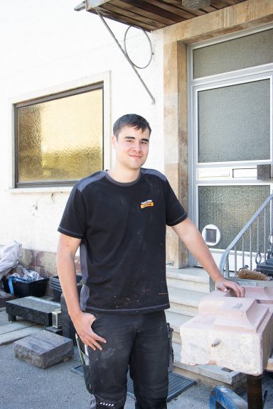 Junger Handwerker steht neben einem Baustellenbereich mit Werkzeug und Materialien.