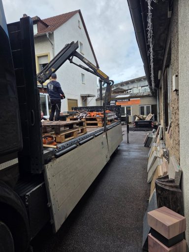 Ein Lkw entlädt Materialien in einer schmalen Gasse zwischen Gebäuden.
