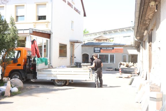 Lkw lädt Baumaterial in einer engen Gasse zwischen Gebäuden.
