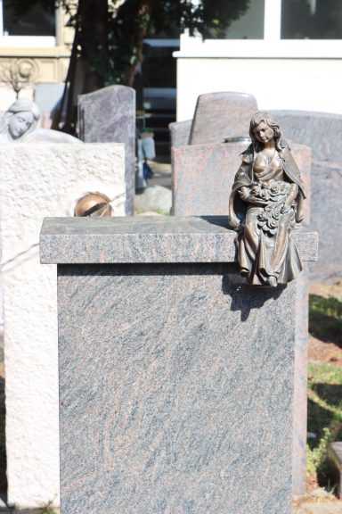 Grabstein mit Statue eines sitzenden Engels und dekorativen Elementen.
