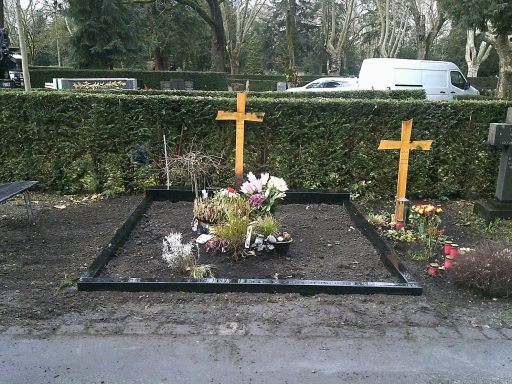 Grabstätte mit zwei hölzernen Kreuzen und frischen Blumenarrangements.