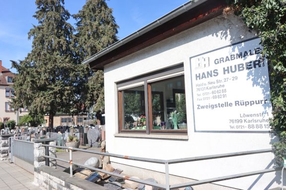 Blick auf das Gebäude der Grabpflege Hans Huberti mit Garten und Bäumen im Hintergrund.