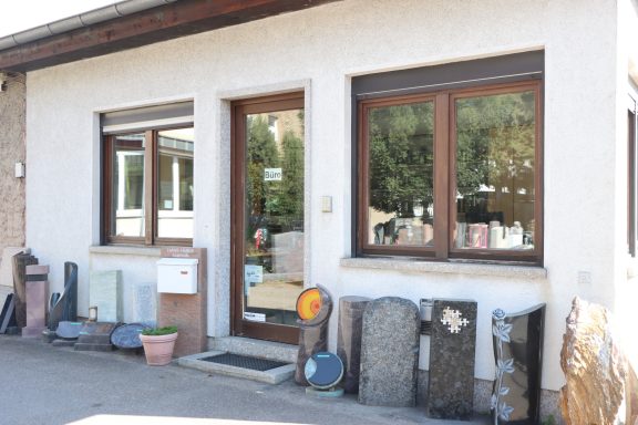Hauseingang mit großen Fenstern und Steinen im Vordergrund.