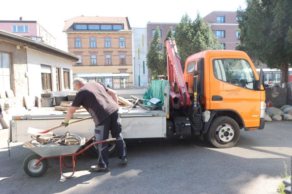 Arbeiter belädt einen Lkw mit Baumaterialien neben einer Schubkarre.