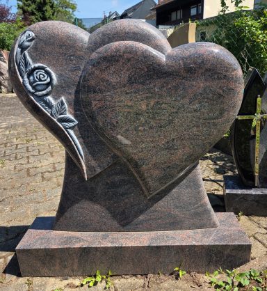 Zwei stilisierte Herzen aus schwarzem Granit mit einer eingravierten Rose.