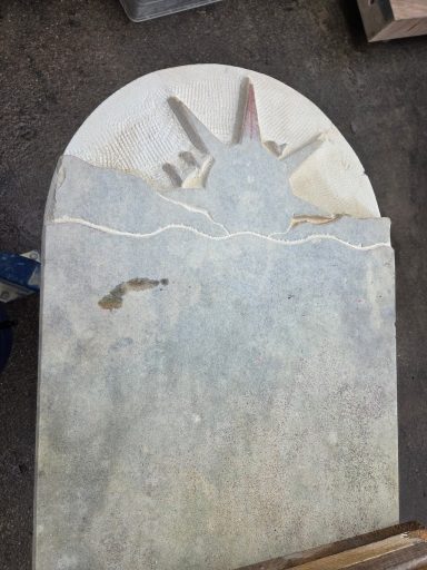Steinplatte mit Relief eines Sonnenaufgangs über Wellen.