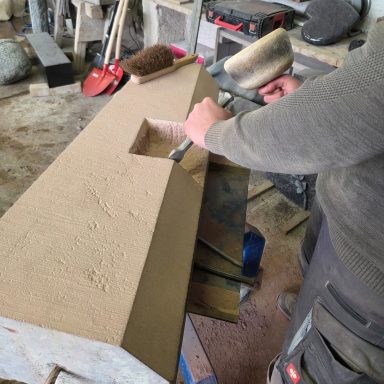 Ein Handwerker bearbeitet einen Block aus Stein mit einem Meißel und Hammer.