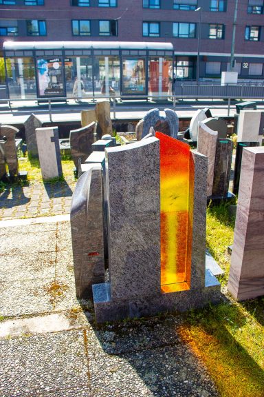 Granitstele mit einer orangefarbenen Lichtdurchlassöffnung auf einem Friedhof.