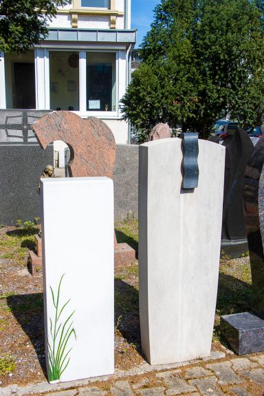 Zwei Schneckenfiguren aus Stein in einem Garten, umgeben von Pflanzen und Gebäuden.
