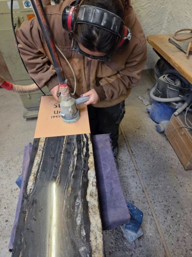 Person arbeitet an einem Holzstück mit einem Router in einer Werkstatt.