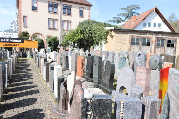 Reihe von Grabsteinen in einem Friedhof mit historischen Gebäuden im Hintergrund.